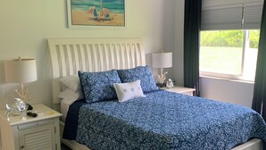 Ein Schlafzimmer mit Bett, Nachttischen, Deckenventilator, einem Gemälde und einem Fenster mit Vorhängen.