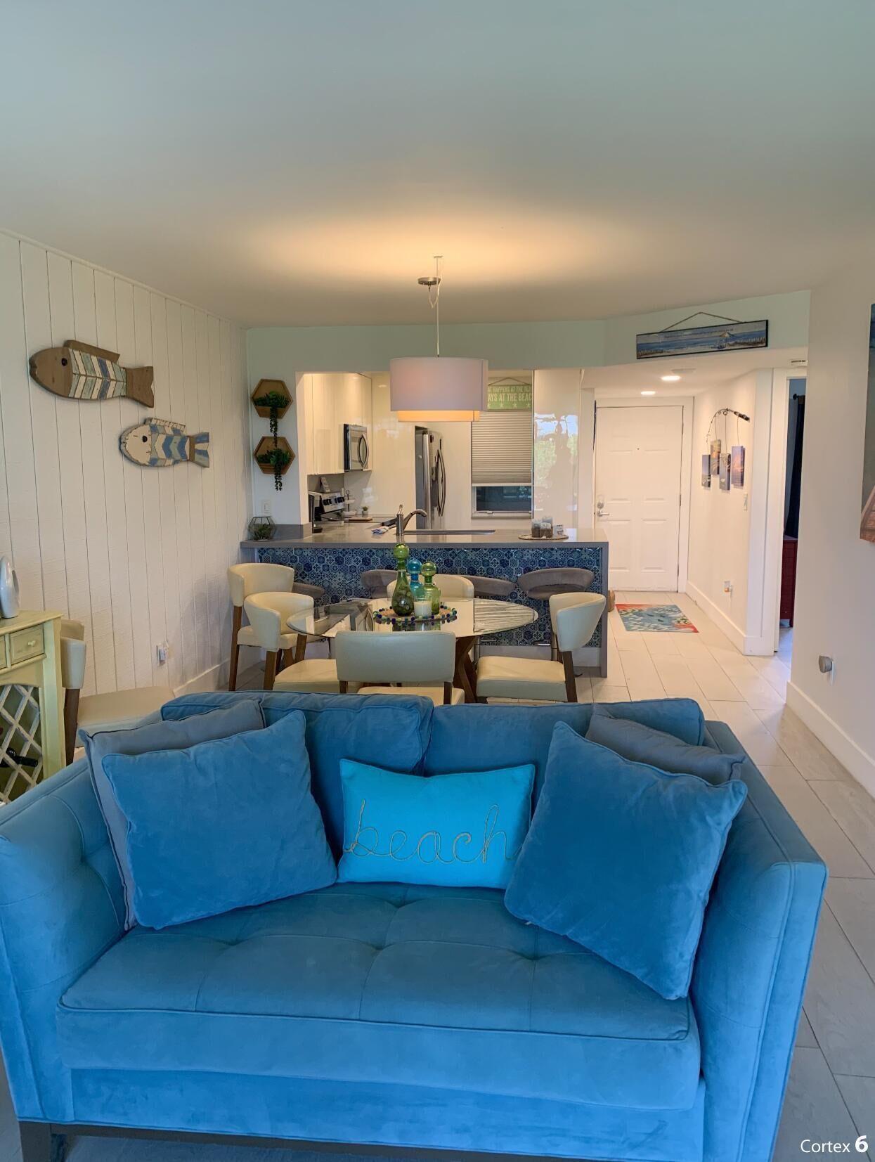 A living room with a blue sofa, a dining area with a table and chairs, and a kitchen in the background.