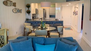 Ein Wohnzimmer mit einem blauen Sofa, einem Essbereich mit Tisch und Stühlen und einer Küche im Hintergrund.