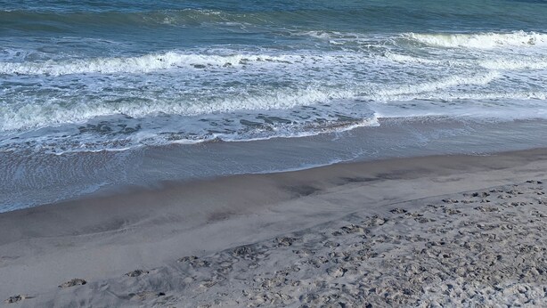 Ein Strand mit Wellen, einem klaren Himmel und weiter Ferne.