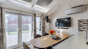 Una cocina moderna con un televisor grande, un comedor con sillas y una puerta corrediza de vidrio que da a un patio trasero.