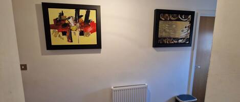 A hallway with two framed abstract paintings, a radiator, and a trash bin.