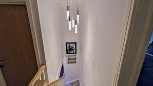 Una escalera estrecha con barandilla de madera y una lámpara en el techo.