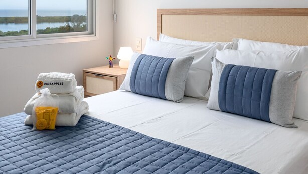 A hotel room with a bed, a nightstand, an air conditioning unit, and a window with a view of the ocean. - Luxury in Barra da Tijuca Near the Olympic Park Av806 (Rio de Janeiro)