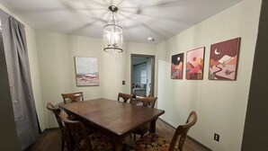 A dining room with a wooden table and chairs, a chandelier, and three framed artworks on the wall. - The Boho Blast of Winston-Salem (Winston-Salem)