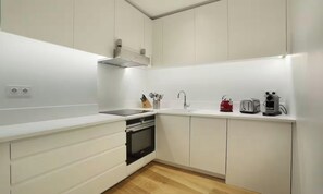 A modern kitchen with white cabinetry, a built-in oven, a sink, and a countertop with various appliances.