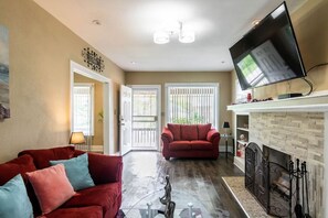 A living room with a red sofa, a fireplace, a TV, and a door leading outside.