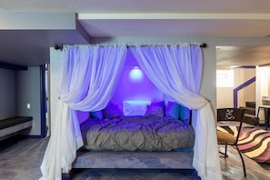 A bed with a canopy, a small seating area, and a staircase leading to another room.