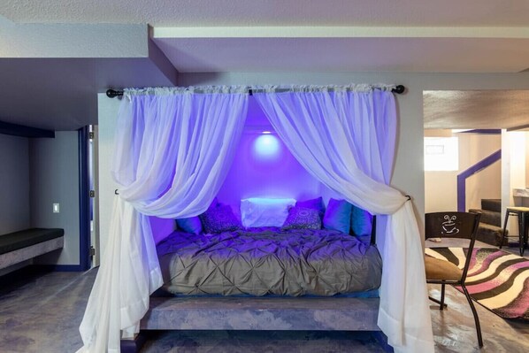 A bed with a canopy, a small seating area, and a staircase leading to another room.