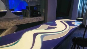 Baaritiski, jonka työtaso on kaareva, sekä kahvinkeitin ja televisio.