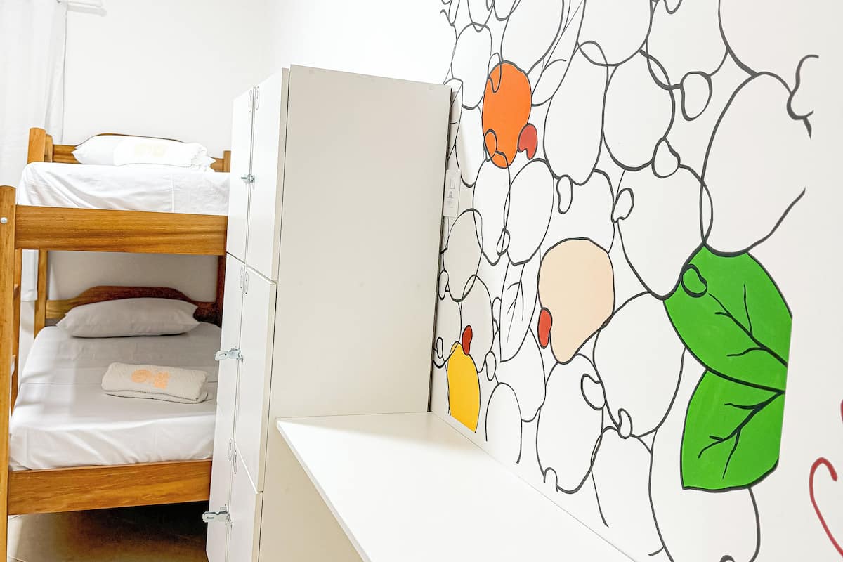 A bunk bed with a desk attached, a white wall with a colorful abstract mural, and a white tiled floor.