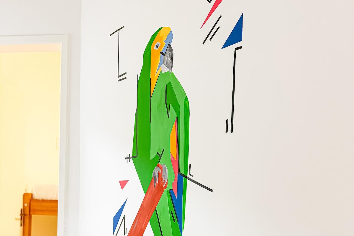 A colorful abstract art piece on a white wall, featuring a parrot and geometric shapes.