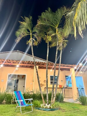 A building with a tiled roof, a door, and a window. There are palm trees in front of the building. - Caju Villa  (Aracaju)