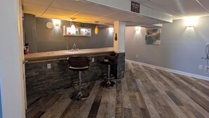 Uma área de bar com bancada de pedra, dois banquinhos e iluminação pendente.