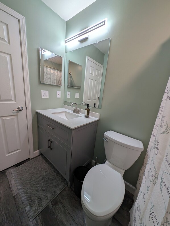 Un baño con inodoro blanco, lavamanos con espejo y cortina de ducha con texto.