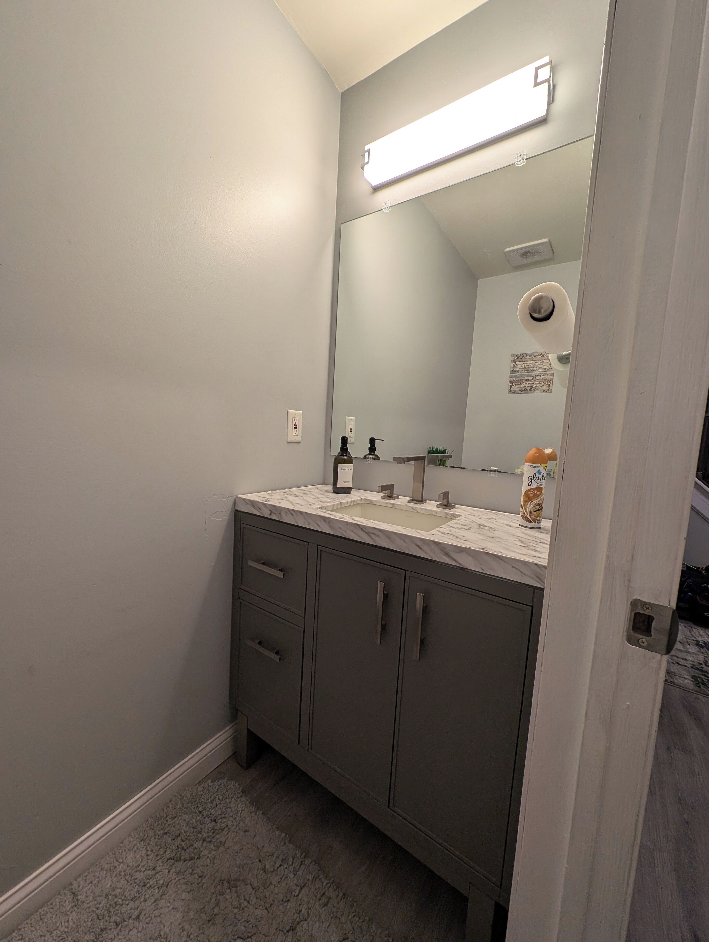 A bathroom with a marble countertop, a large mirror, a towel dispenser, and a bottle of hand soap.