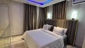 A modern bedroom with a large bed, a headboard, and a ceiling with blue LED lighting. - Casa- Grey Apartments (Abuja)