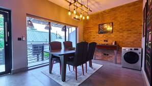 A modern kitchen with a brick wall, a dining area with a table and chairs, and a washing machine. - Casa- Grey Apartments (Abuja)