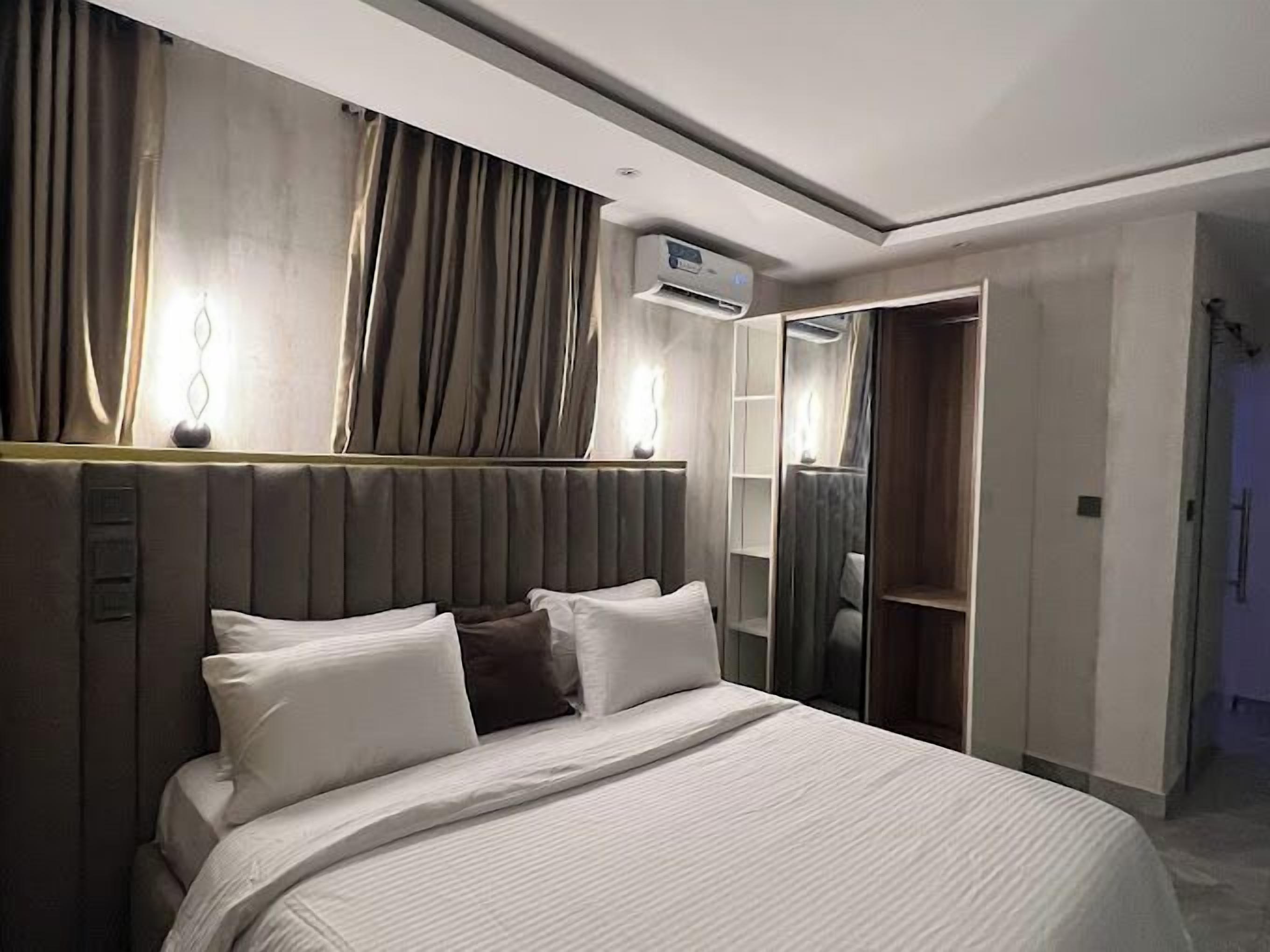 A modern hotel room with a large bed, a built-in wardrobe, and an air conditioning unit.