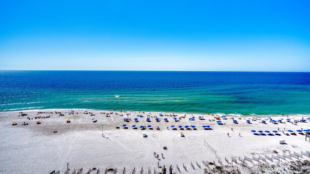 A beach with rows of blue and yellow umbrellas, a sandy shore, and the ocean in the background. - Phoenix IV 4112 (Orange Beach)