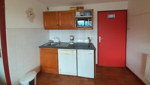 Una cocina compacta con armarios de madera, microondas integrado y una puerta roja.