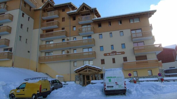 Un hotel de varios pisos con balcones, una entrada cubierta y el suelo cubierto de nieve.