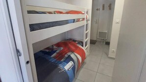 A small, narrow room with a bunk bed, a door, and a small window.