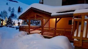 A wooden chalet with a covered porch and a snow-covered roof, surrounded by a snowy landscape.