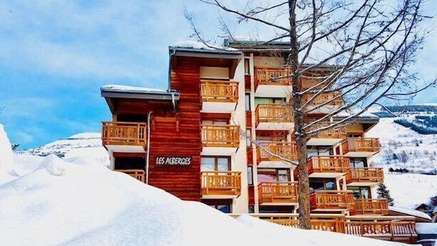 A multi-story hotel with wooden balconies and a sign reading "LES ALBERGES".