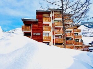 Un hôtel à plusieurs étages, doté de balcons en bois et d’une enseigne indiquant « LES ALBERGES ».