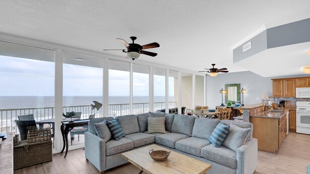 A spacious living area with a large gray sectional sofa, a wooden coffee table, and a view of the ocean.