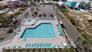 An aerial view of a resort with a large pool, multiple buildings, and a beach in the background.