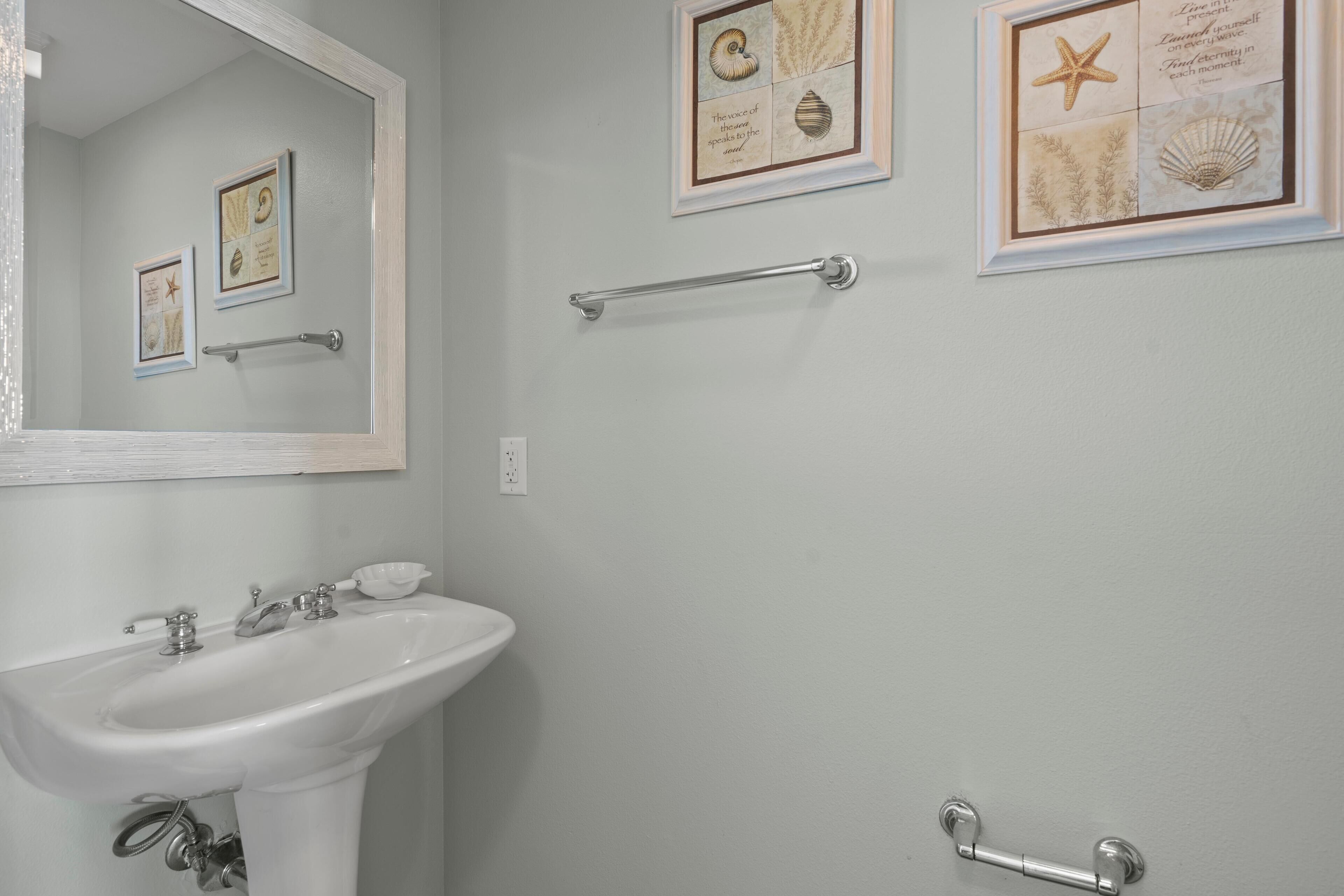 A bathroom with a white sink, a mirror, and three framed pictures on the wall.