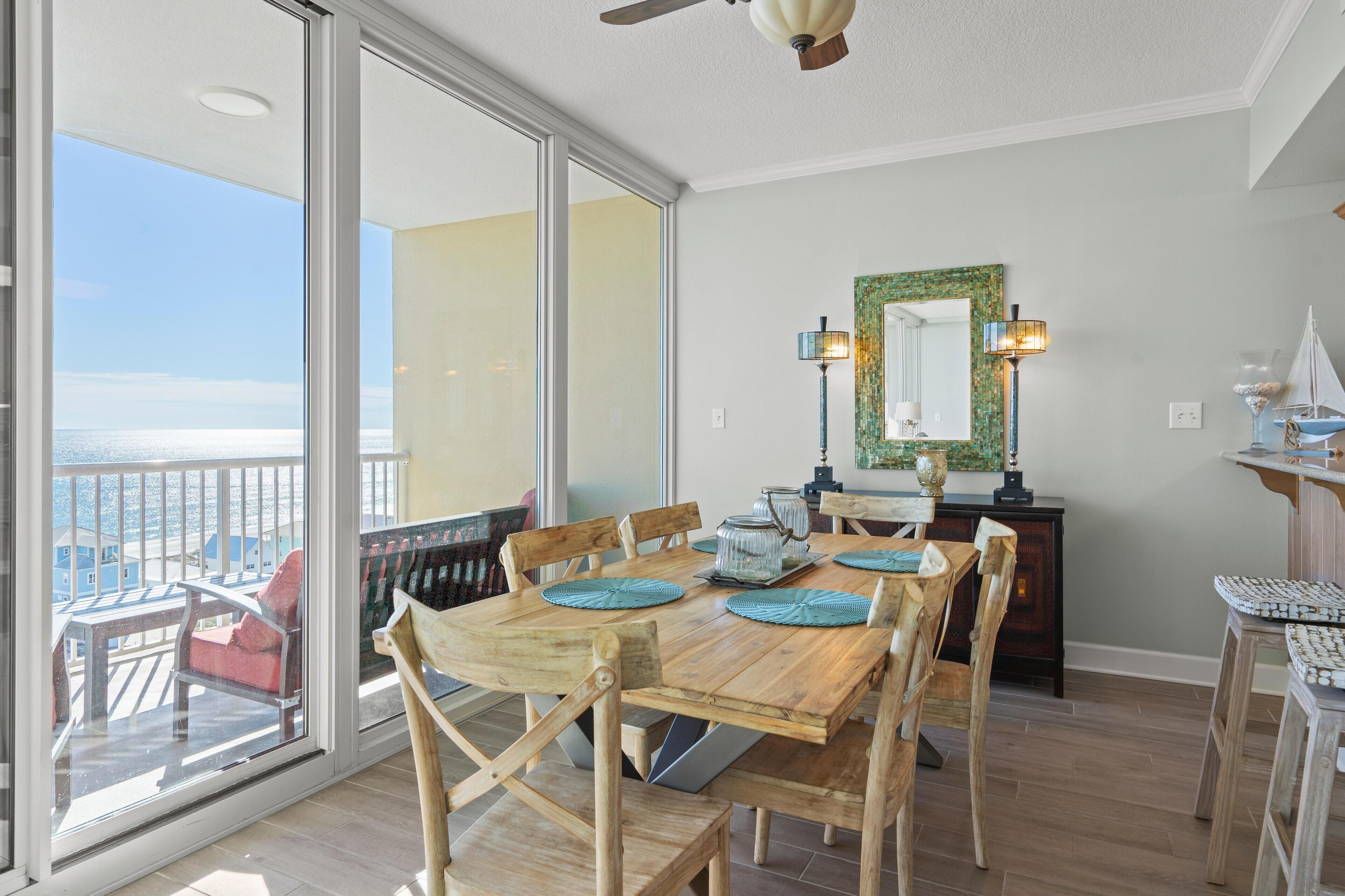 A dining area with a wooden table and chairs, a balcony with a view, and a ceiling fan.