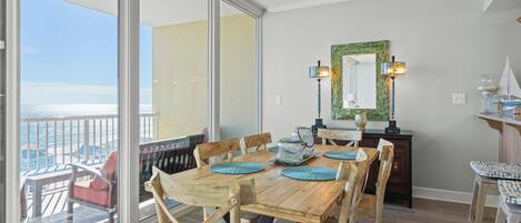 A dining area with a wooden table and chairs, a balcony with a view, and a ceiling fan.
