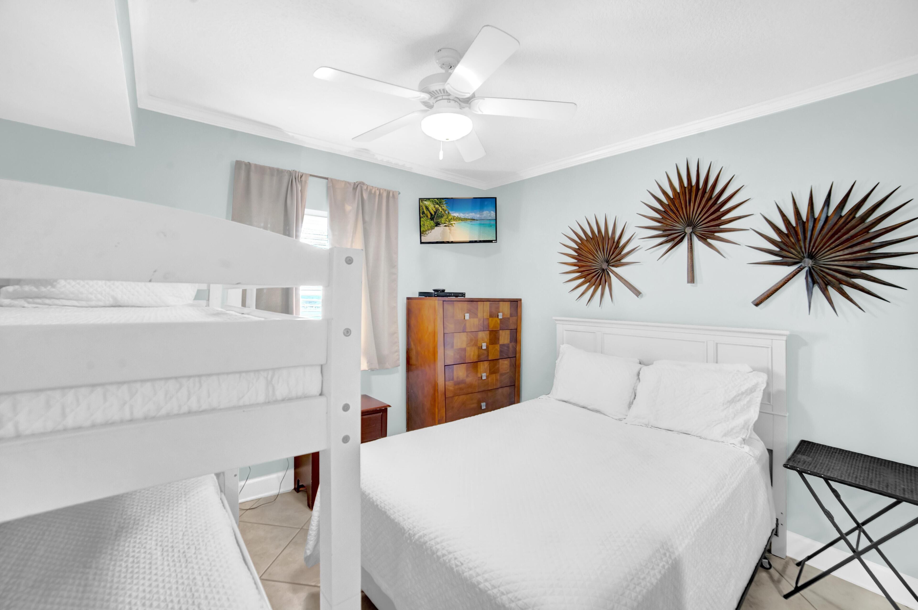 A bedroom with a bunk bed, a single bed, a ceiling fan, a TV, decorative wall art, and a wooden cabinet.