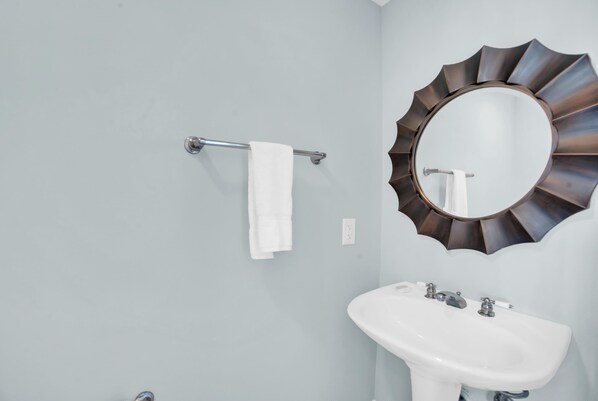 A bathroom with a white sink, a towel rack with a white towel, and a decorative mirror with a unique frame. - Sanibel 1105 (Gulf Shores)