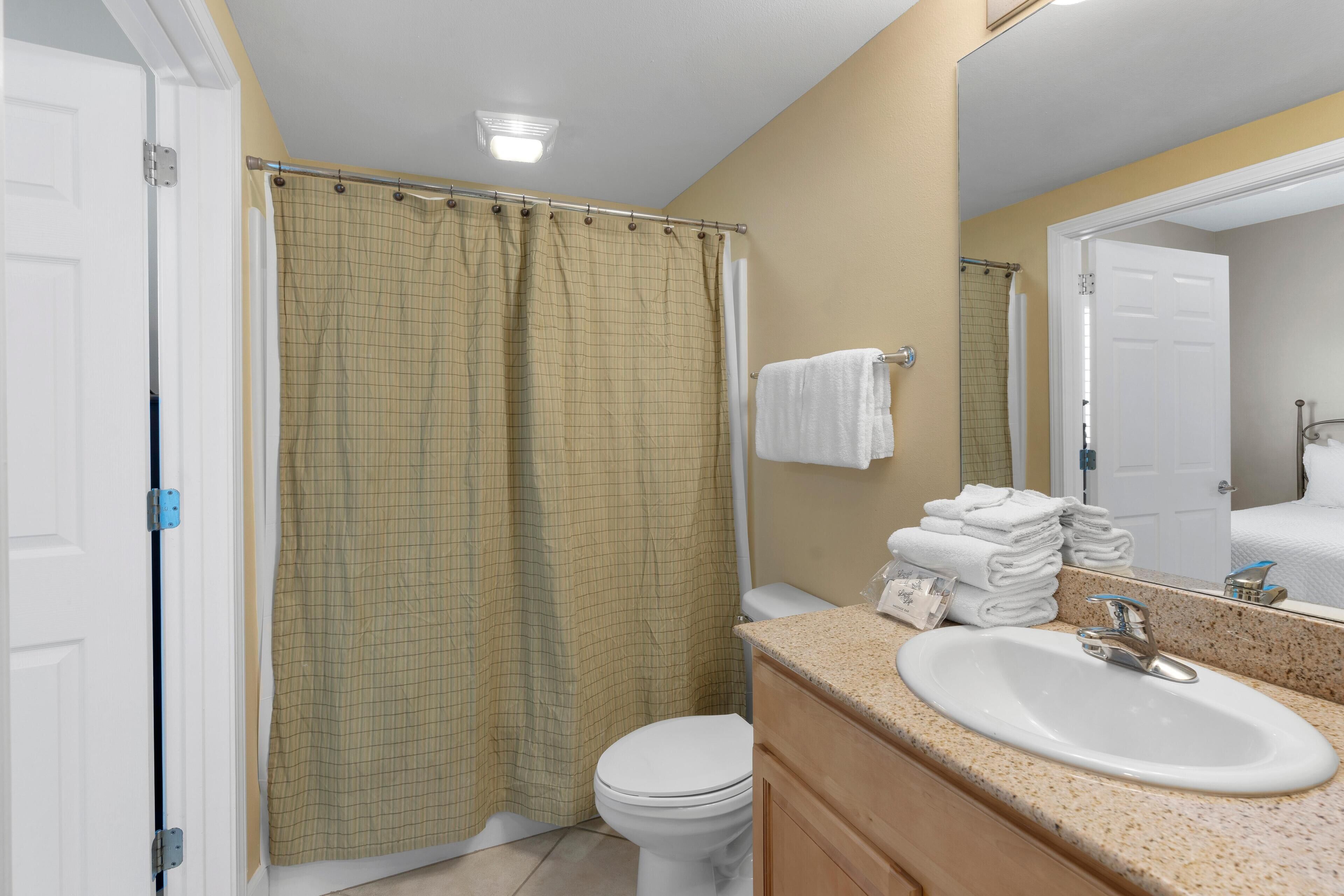 A bathroom with a white toilet, a beige shower curtain, a sink with a mirror, and a towel rack with folded towels.