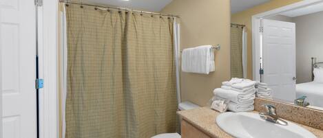 A bathroom with a white toilet, a beige shower curtain, a sink with a mirror, and a towel rack with folded towels.