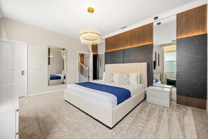Relax in a serene space with a large bed, nightstand, and dresser, complemented by a chandelier and full-length mirror.