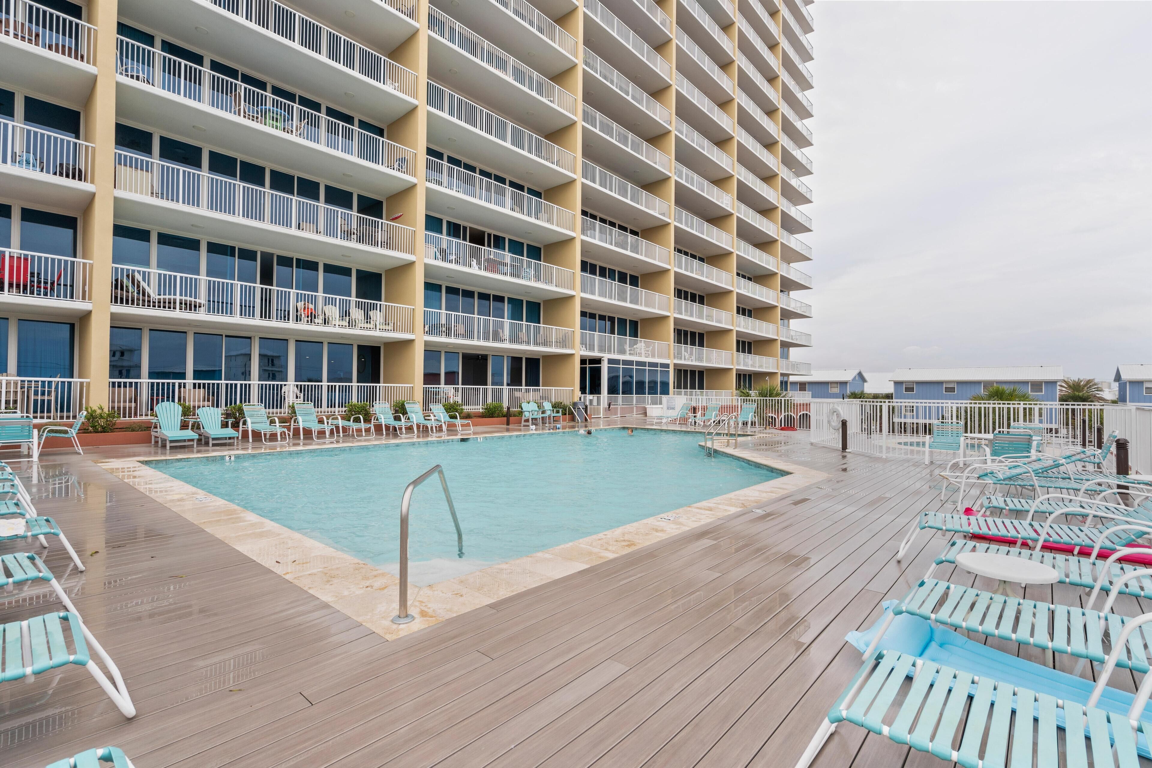 Un espace piscine d’hôtel comprenant une grande piscine, plusieurs balcons et des chaises longues.