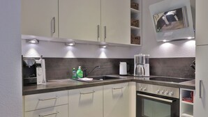 A modern kitchen with a built-in oven, a coffee maker, and a sink. - This enchanting, modern and tastefully furnished 3-room apartment with a covered terrace and a view of the countryside invites you to linger. (Ostseebad Nienhagen)