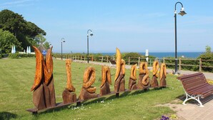 A park with wooden sculptures, a bench, and a view of the sea. - This enchanting, modern and tastefully furnished 3-room apartment with a covered terrace and a view of the countryside invites you to linger. (Ostseebad Nienhagen)