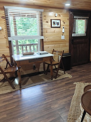 A wooden interior with a desk, chairs, a door, and a window with blinds.