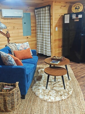 A cozy room with a blue sofa, a small wooden table, a woven basket, and a refrigerator.