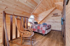 A wooden interior with a bed, a rocking chair, and a 'Welcome' sign.