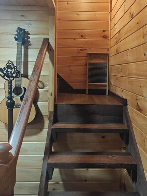 A wooden staircase leading to a loft area with a guitar leaning against the wall.