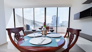Uma área de refeições com uma mesa redonda para quatro pessoas, janelas amplas com vista para a cidade e uma TV de tela plana na parede.