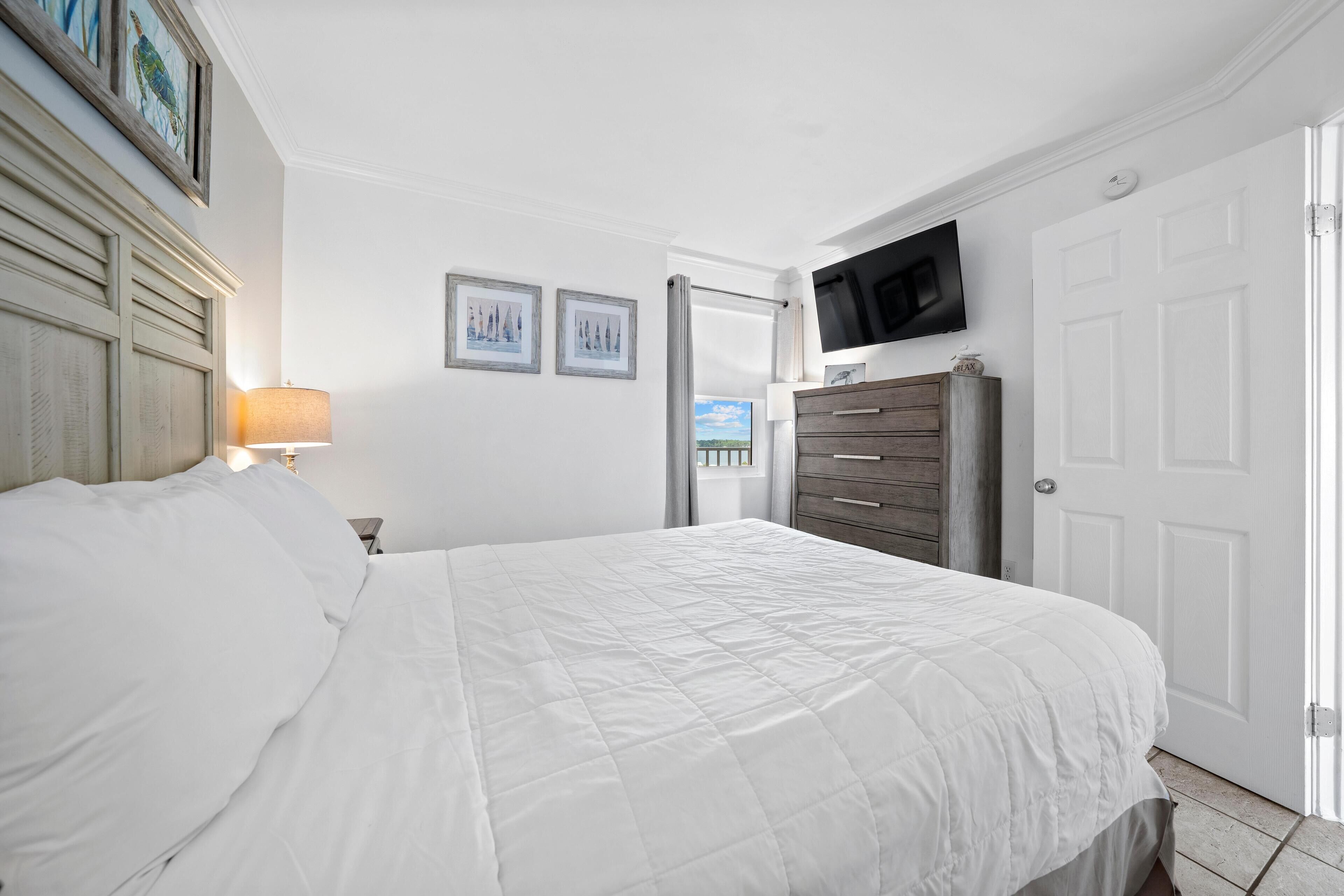 Une chambre à coucher avec un lit, une commode, un téléviseur et des tableaux encadrés accrochés au mur.