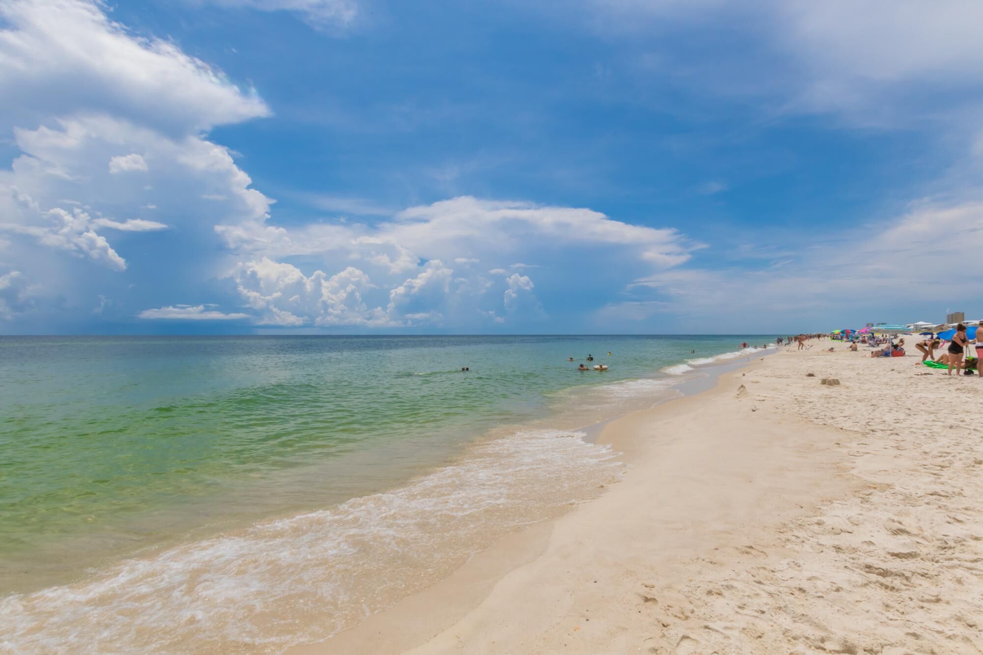 Une plage avec une eau turquoise et limpide, un rivage sablonneux et un ciel partiellement nuageux.